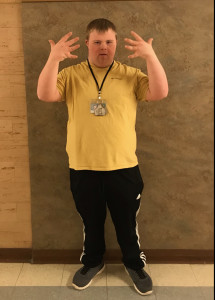 student stands facing camera with hands around his face